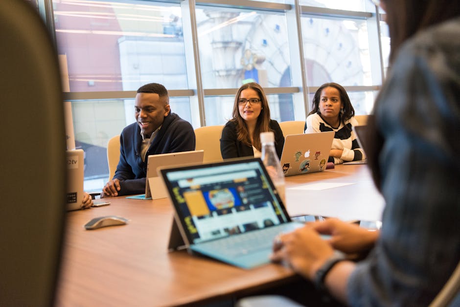 A diverse group of professionals working together on laptops in a modern office meeting room.