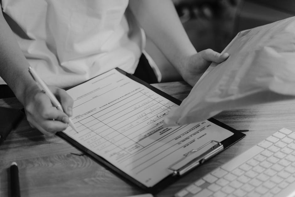 Black-and-white photo of a person writing on a clipboard with a keyboard visible.