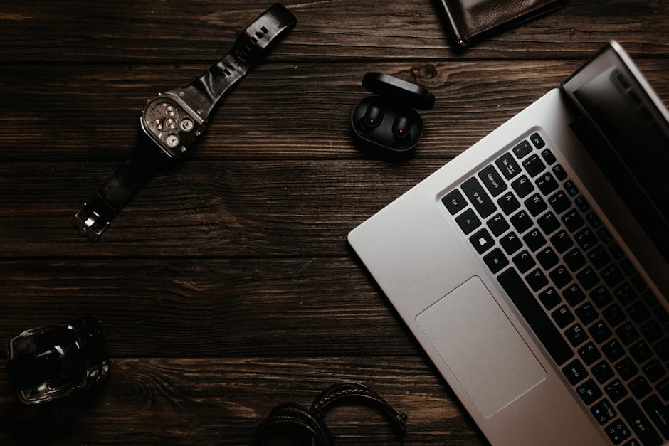 Top view of a sleek workspace featuring a laptop, watch, and earphones on a wooden table.