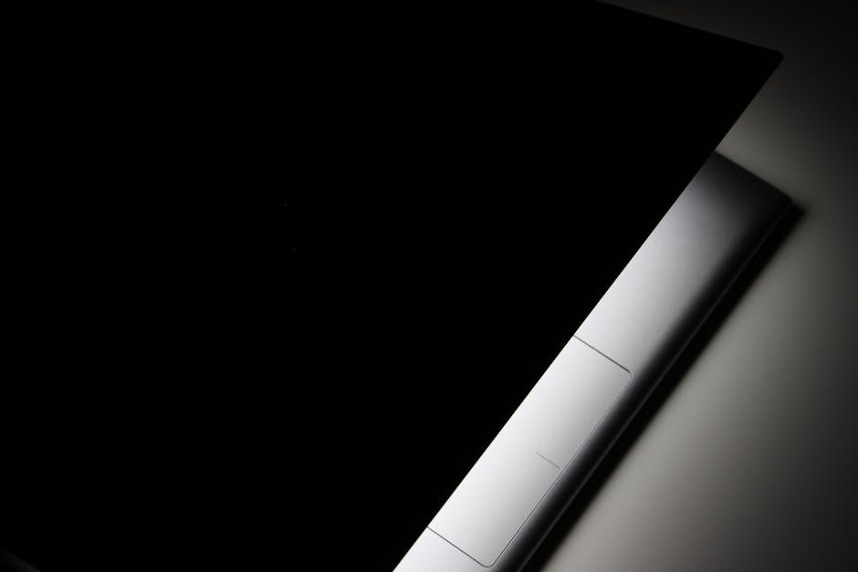 A partial view of a modern laptop closed in shadow, highlighting its sleek design.