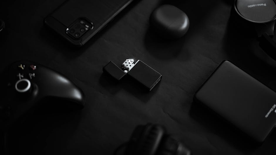 A set of black gadgets and a lighter on a dark surface, showcasing minimalist technology design.
