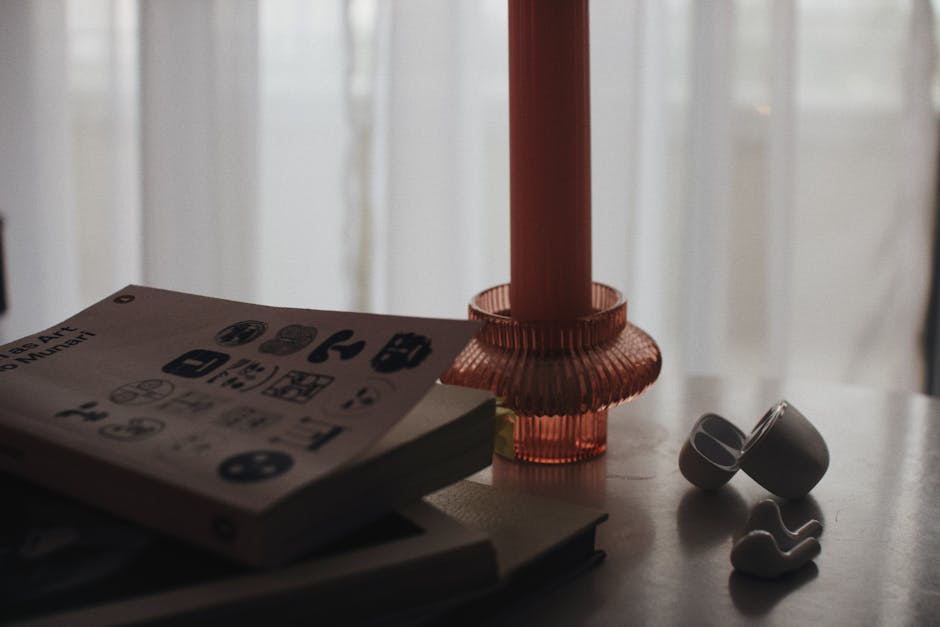 Aesthetic indoor still life with books, a candle holder, and earbuds on a table.