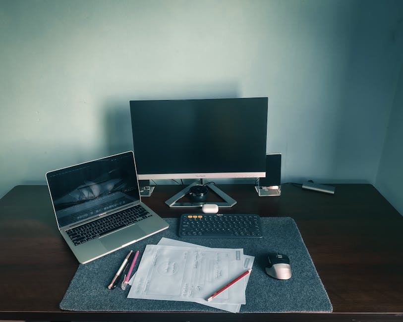Modern home office setup featuring a laptop, monitor, keyboard, and papers on a sleek desk.