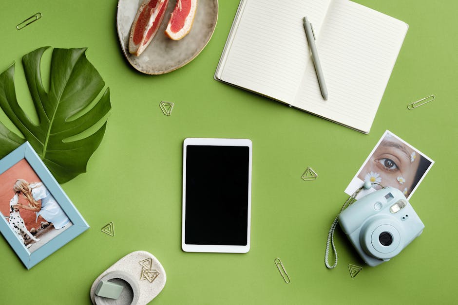 A flat lay featuring stationery, a camera, and a tablet on a green background, perfect for creative concepts.