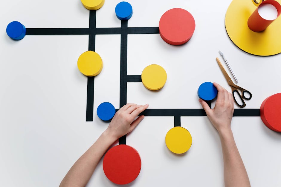 Colorful geometric papercraft shapes arranged creatively on a table with hands and tools.