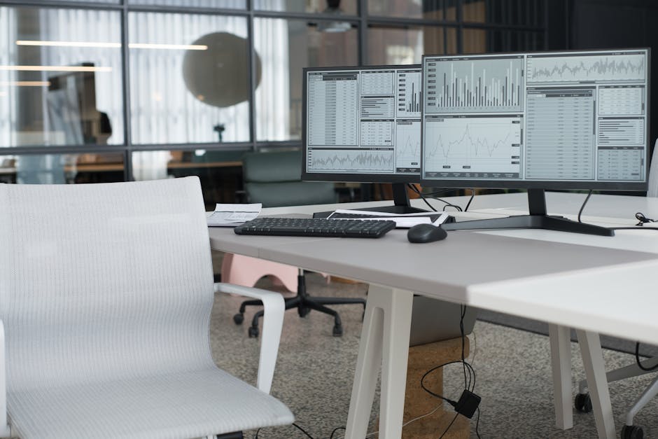 A modern office desk with dual monitors displaying data and an ergonomic chair, perfect for a productive workspace.