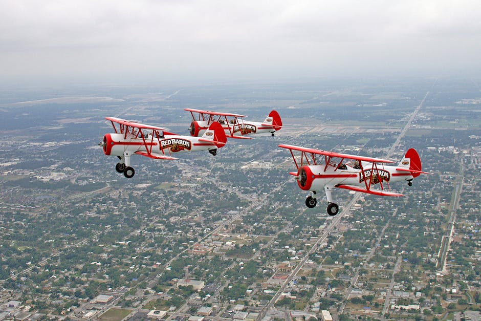Three Red Baron biplanes flying in formation over a Florida city on a cloudy day.