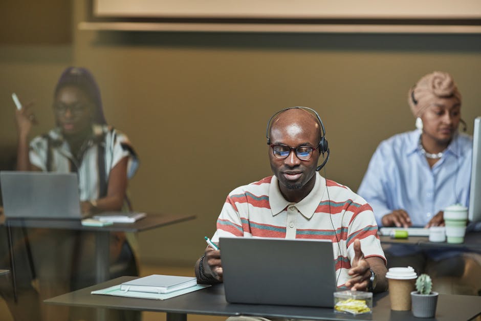 Diverse team collaborating in an office setting with laptops and headsets, focusing on teamwork.