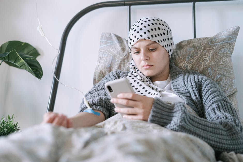 A woman undergoing treatment uses her smartphone for connection and comfort in a clinic room.