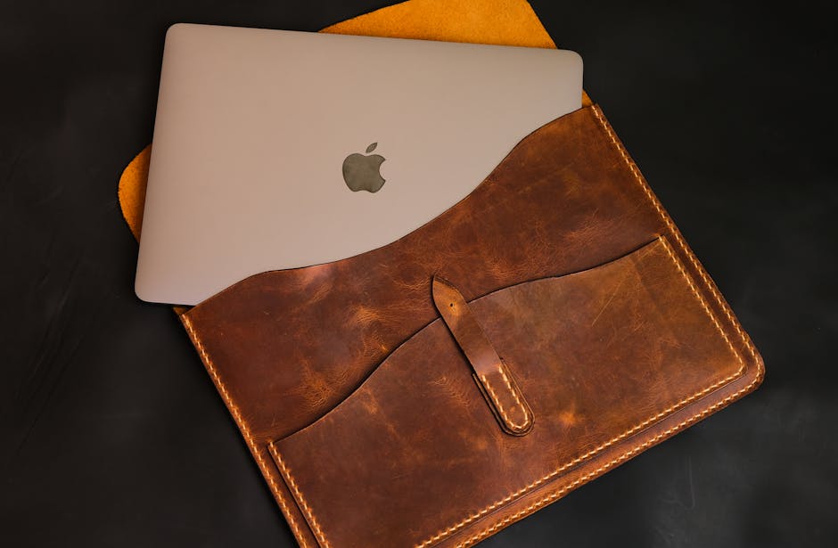 A sleek MacBook partially tucked into a stylish brown leather laptop case.
